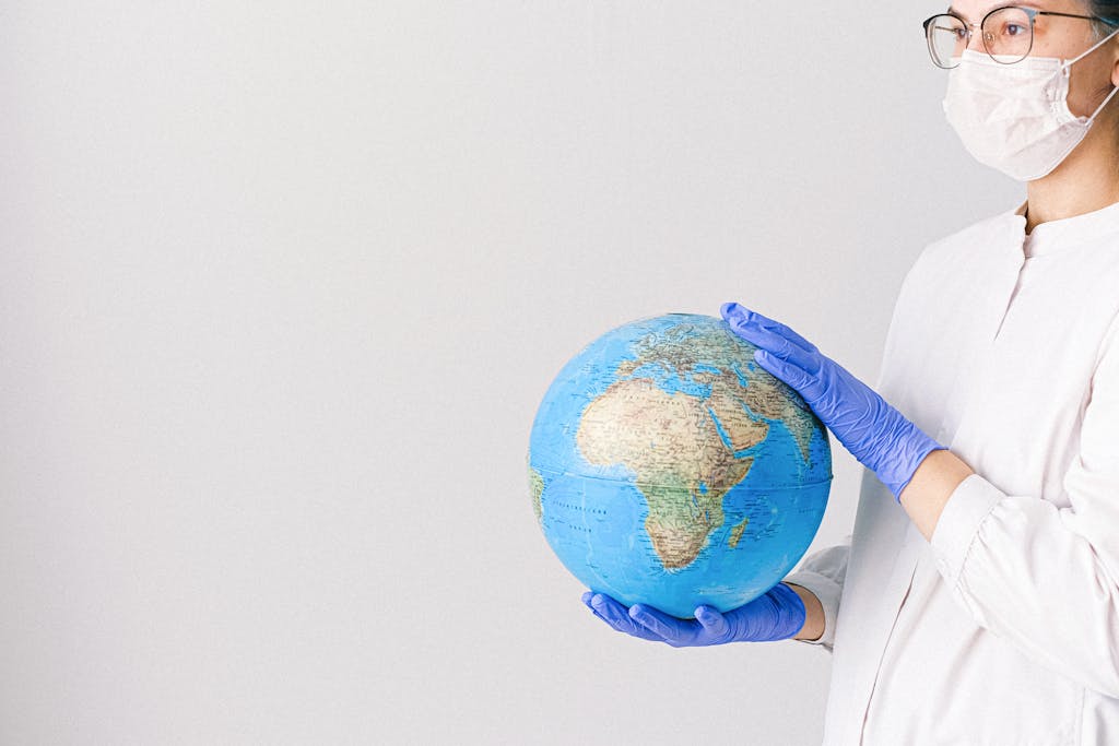 Person With a Face Mask and Latex Gloves Holding a Globe